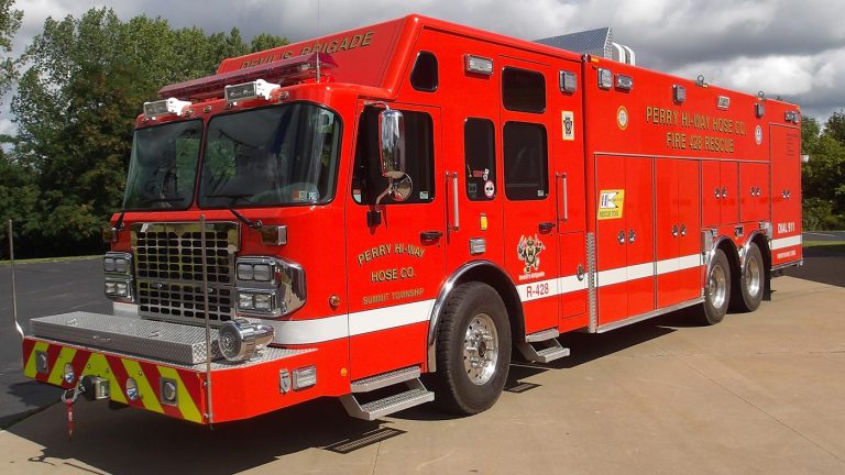 A large red fire rescue truck labeled “Perry Hi-Way Hose Co.” and "Special Operations" is parked on asphalt near trees. The truck has multiple compartments and emergency lights on top.